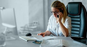 HR professional reviewing healthcare documents while speaking on the phone, illustrating rising employer healthcare costs and administrative burden.